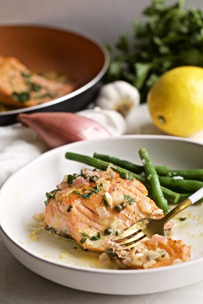 Salmon Piccata with green beans on a plate with a fork.