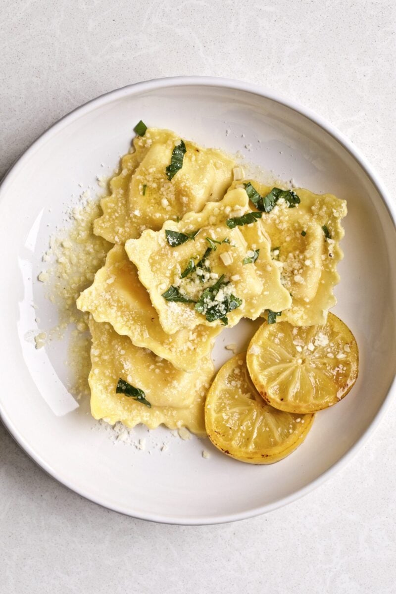 Lobster Ravioli with Lemon Brown Butter Sauce on a plate with a side of grilled lemons ready to eat!.