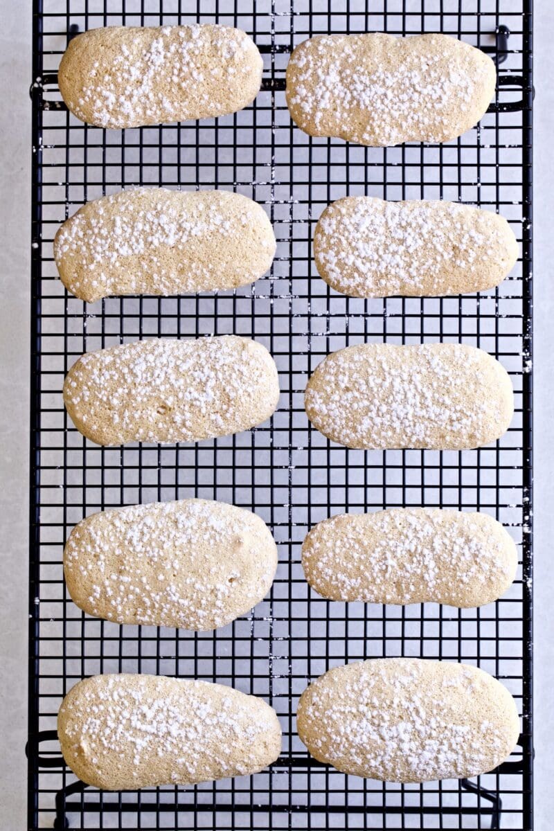 Homemade Italian Ladyfinger Recipe (Savoiardi) cooling on a black cookie cooling rack