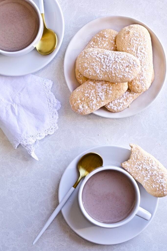 Plate of Italian Ladyfinger cookies and a cup of hot chocolate with a spoon and napkin.