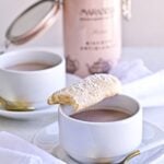 Homemade Italian Ladyfinger Recipe (Savoiardi). Two cups of homemade hot chocolate with a plate of the ladyfinger cookies and an old fashioned white napkin. Ready to eat for breakfast or snack!