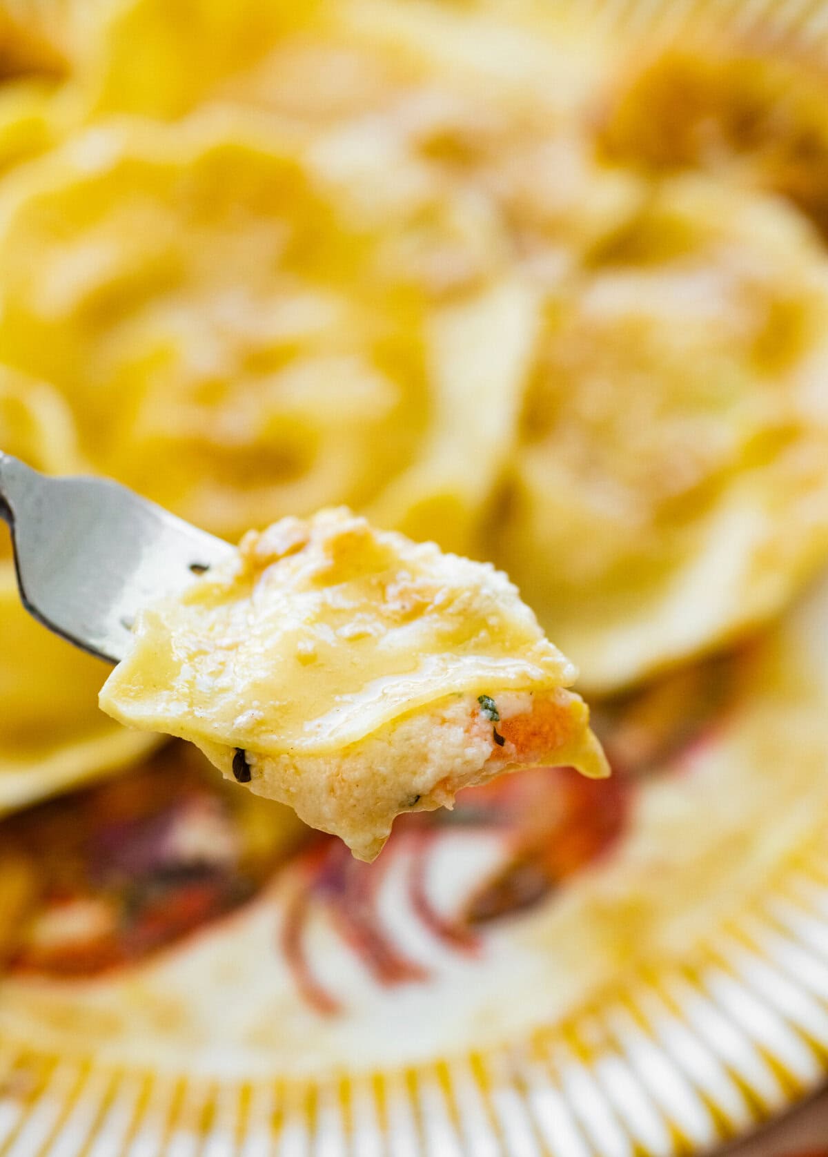 A bite of lobster ravioli in sauce on a fork held up over a plate.