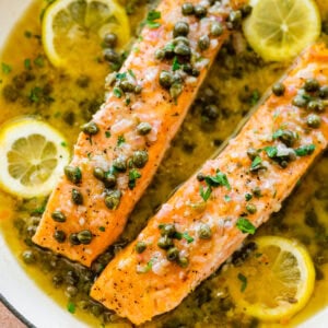 Salmon with lemon caper sauce in a bowl with lemon slices.