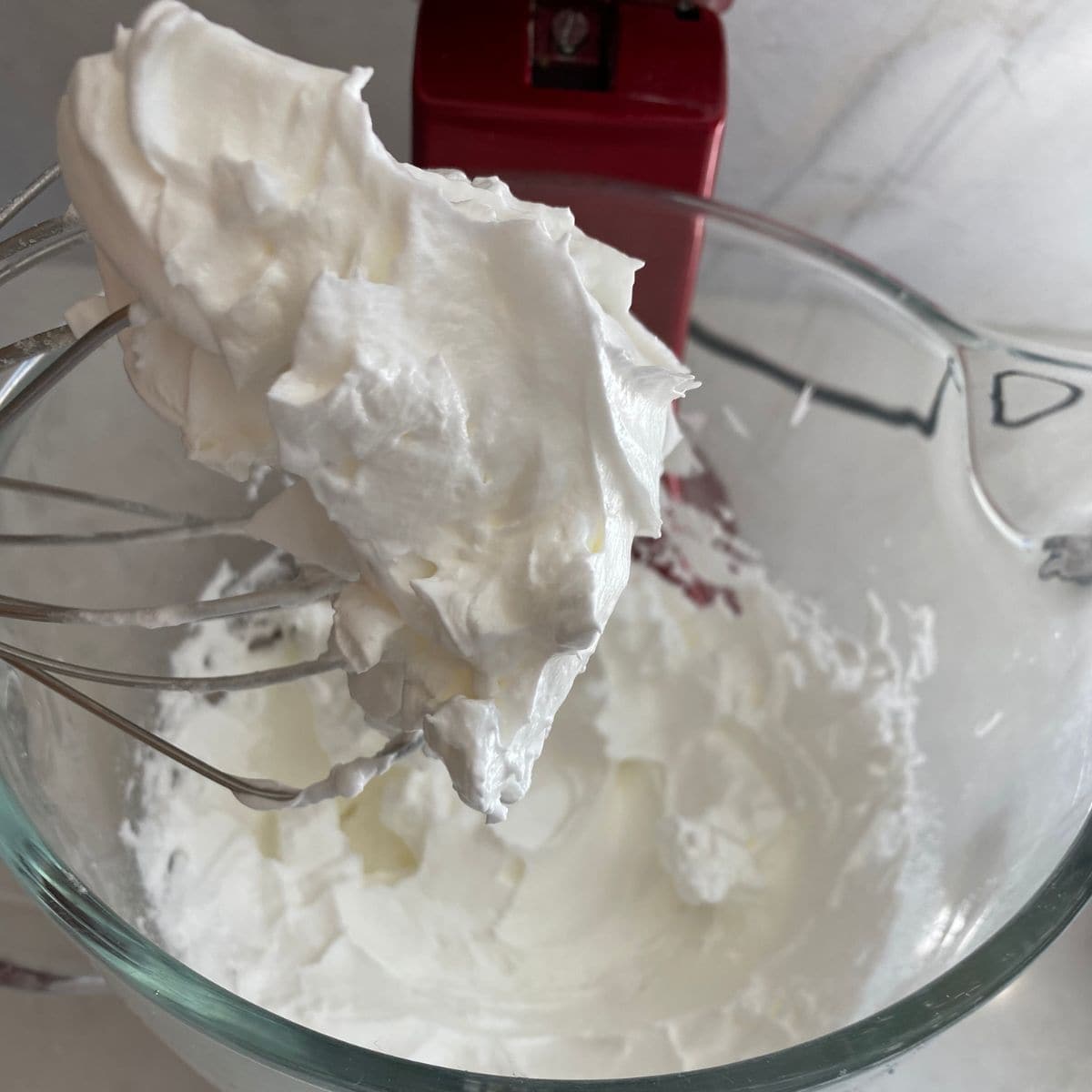 Egg whites beaten to stiff peaks on a beater held up above a bowl of more. 
