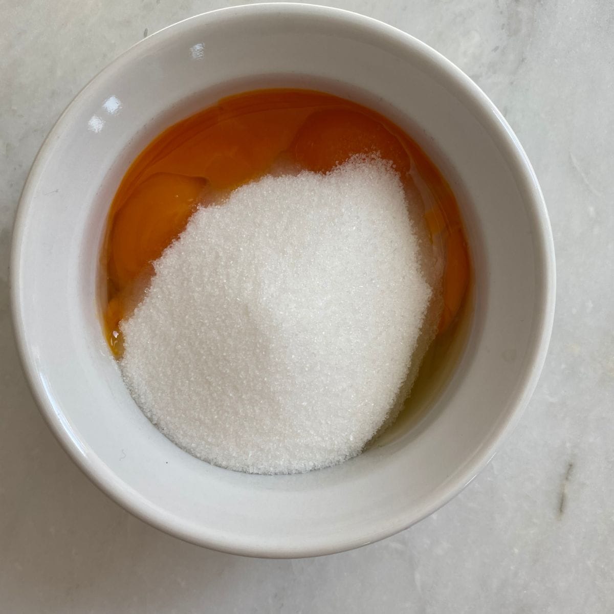 Sugar added to a bowl with the egg yolks. 
