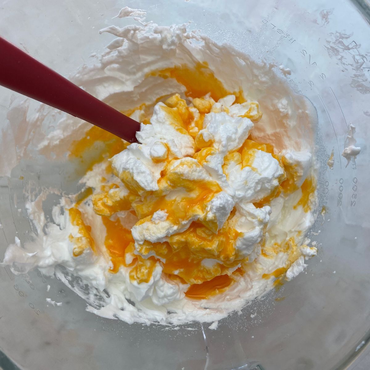 Adding the egg yolk mixture to the bowl of egg whites. 
