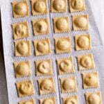 Filled and finished ravioli lying in a row on parchment paper.