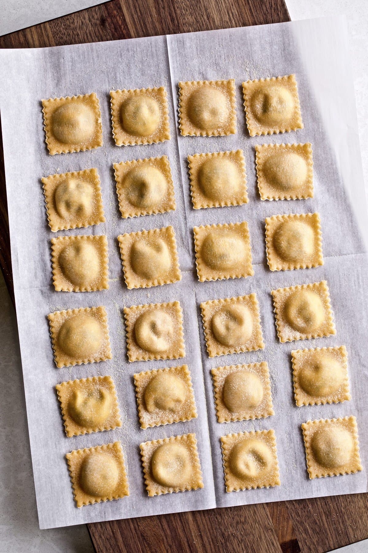 Filled and finished ravioli lying in a row on parchment paper.