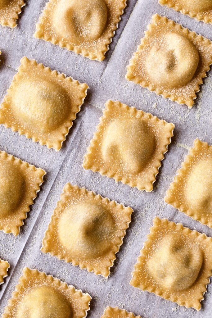 Filled and finished ravioli lying in a row on parchment paper. Marco close up shot.