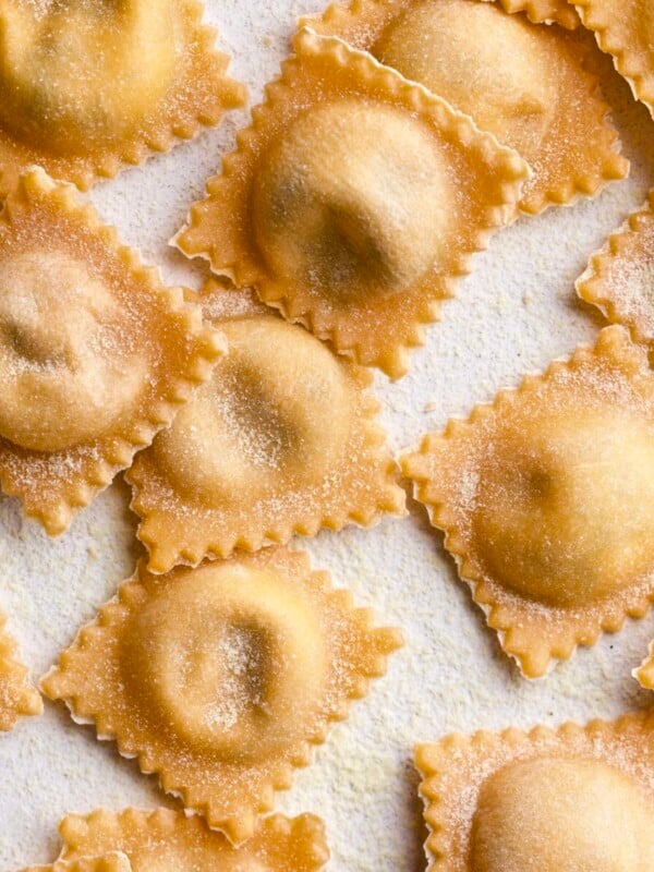 Filled and finished ravioli lying in a row on parchment paper.