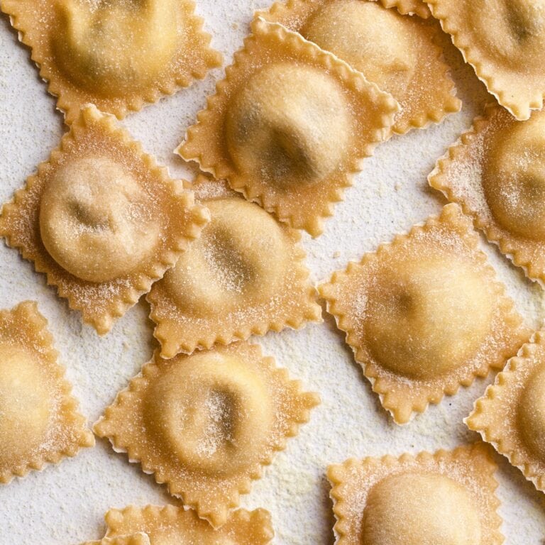 Filled and finished ravioli lying in a row on parchment paper.