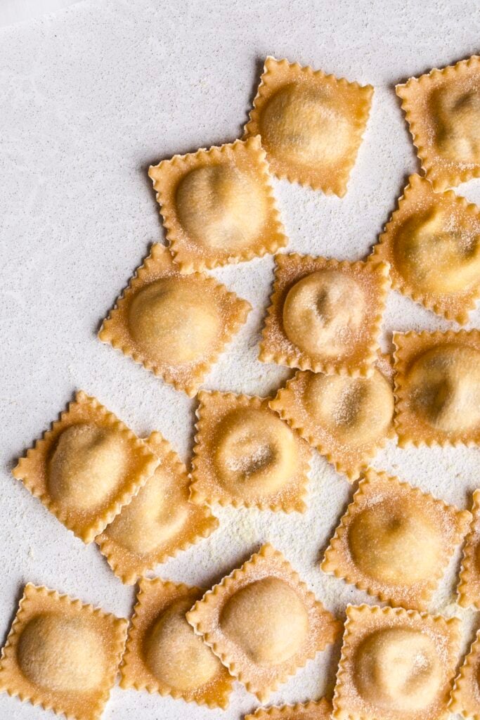 Filled and finished ravioli lying in a row on parchment paper.