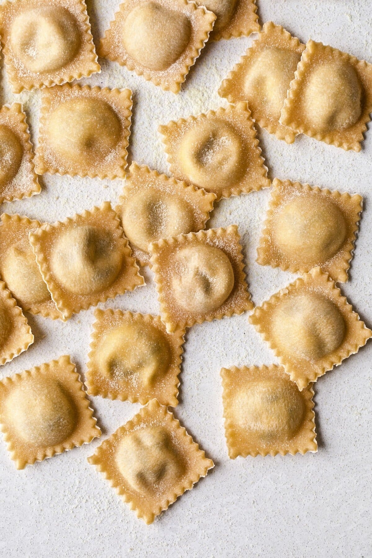 Filled and finished ravioli lying in a row on parchment paper.