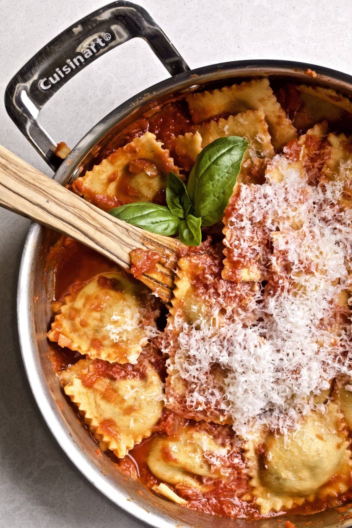 homemade ravioli in red sauce in a pan with a wooden serving utensil.