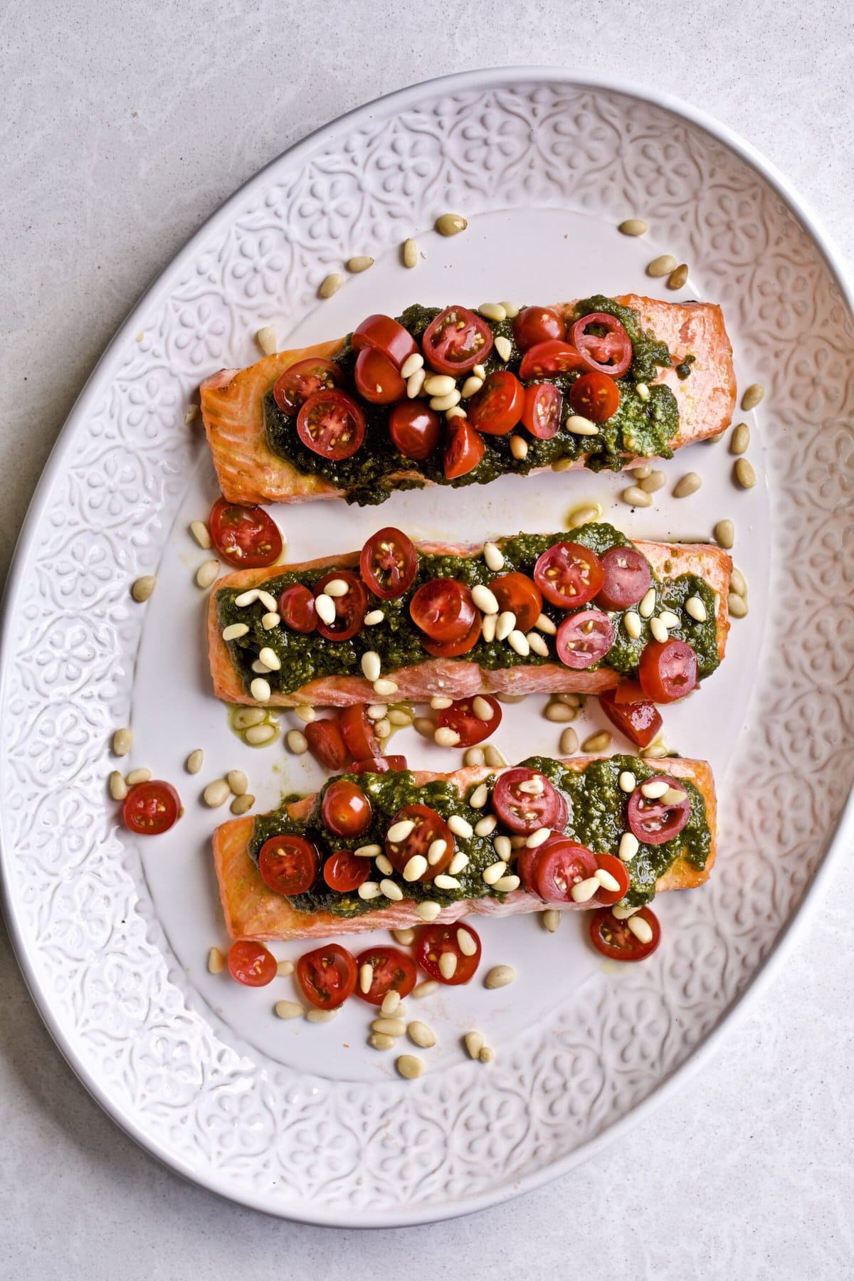 Salmon on a plate with pesto, tomatoes, and garnish.