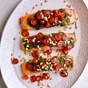 beautifully plated salmon. Three fillet on a platter with pestoover the top, cheery tomatoes, and pine nuts!