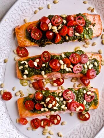 beautifully plated salmon. Three fillet on a platter with pestoover the top, cheery tomatoes, and pine nuts!