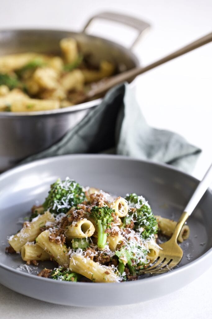 Broccoli Pasta with Sausage Recipe (Italian)- on a plate with a fork. Pan in the background.