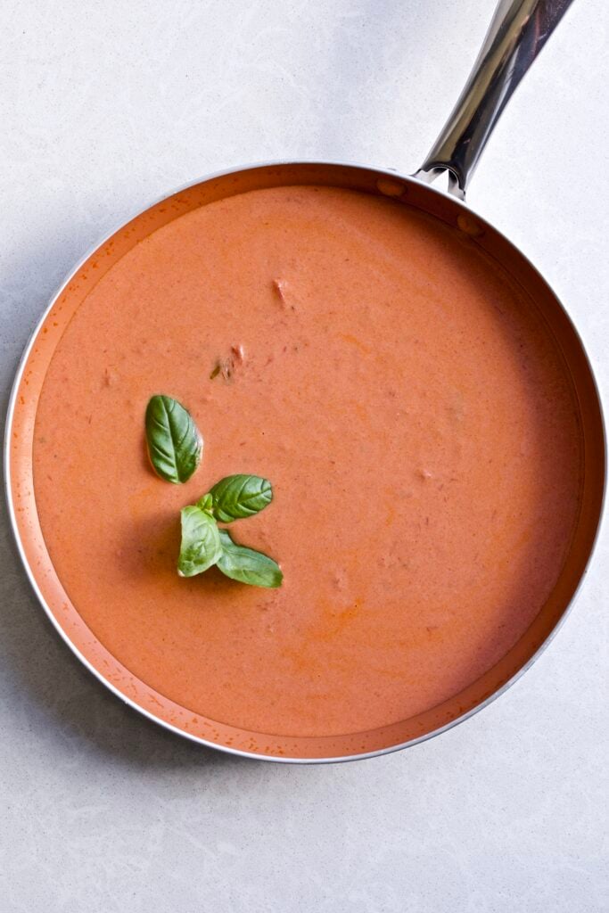 Finished sauce in pan. A pretty pink sauce with a leaf of basil for decoration.