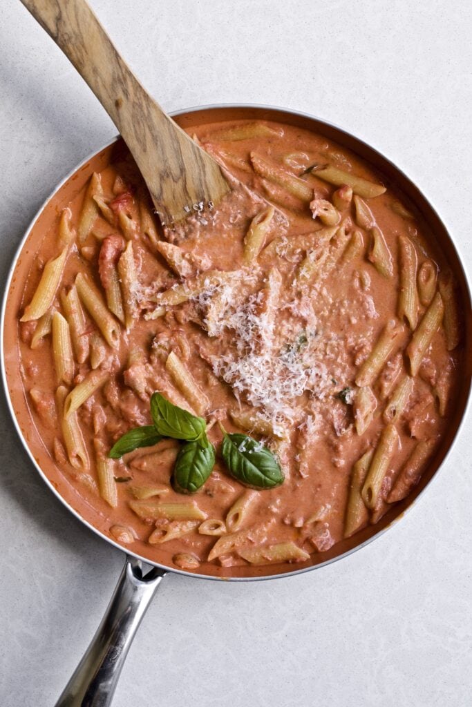 Pasta and sauce are tossed in a pan to combine. Photo of finished dish in pan.