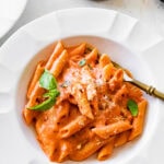 pink pasta in a white bowl ready to eat. Basil on top as garnish.