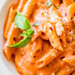 pink pasta in a white bowl ready to eat with a fork.