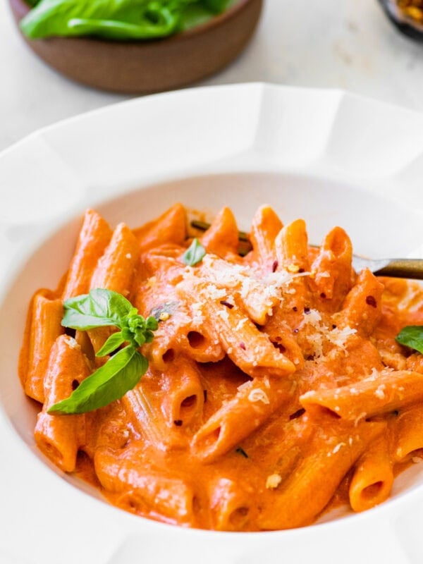 pink pasta in a white bowl ready to eat with a fork.