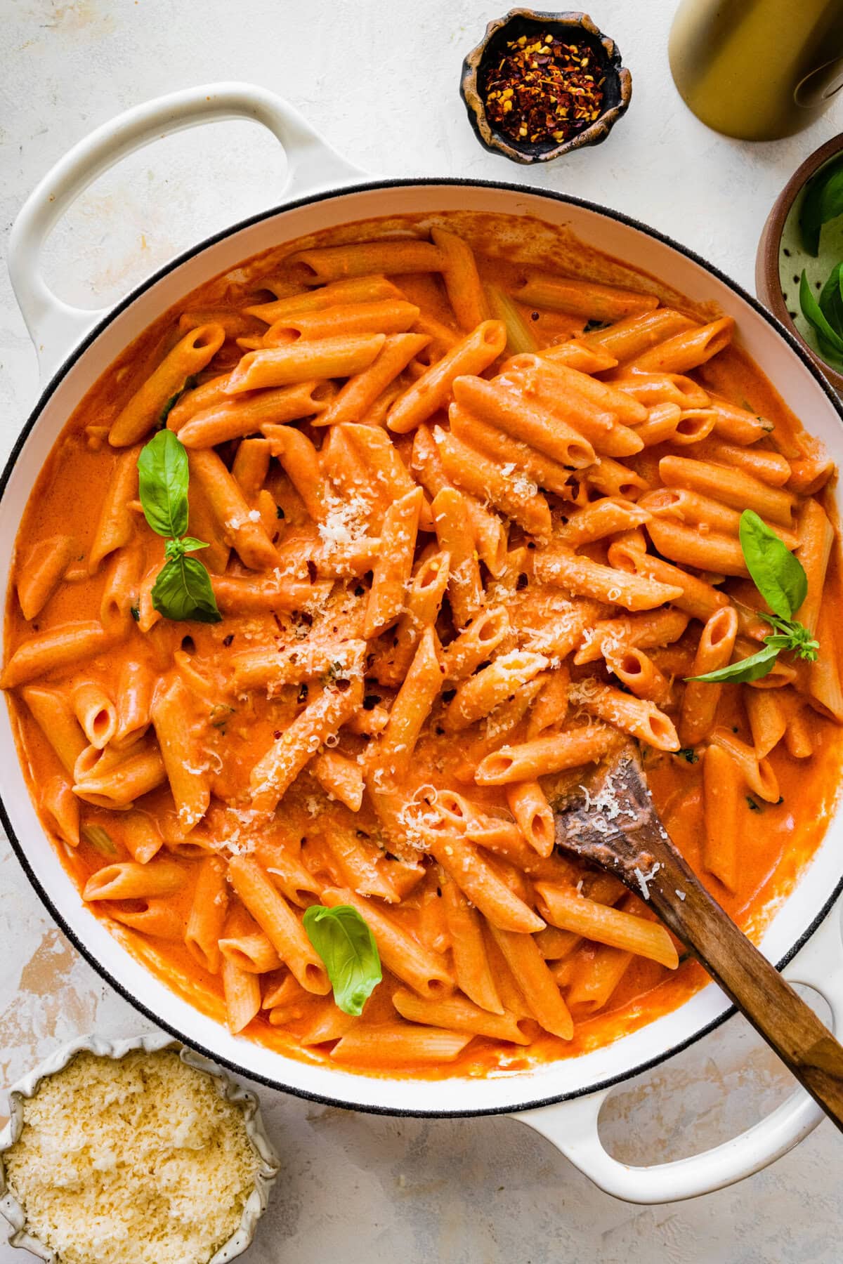 pink sauce penne pasta in the pan with the sauce and basil leaves on top.