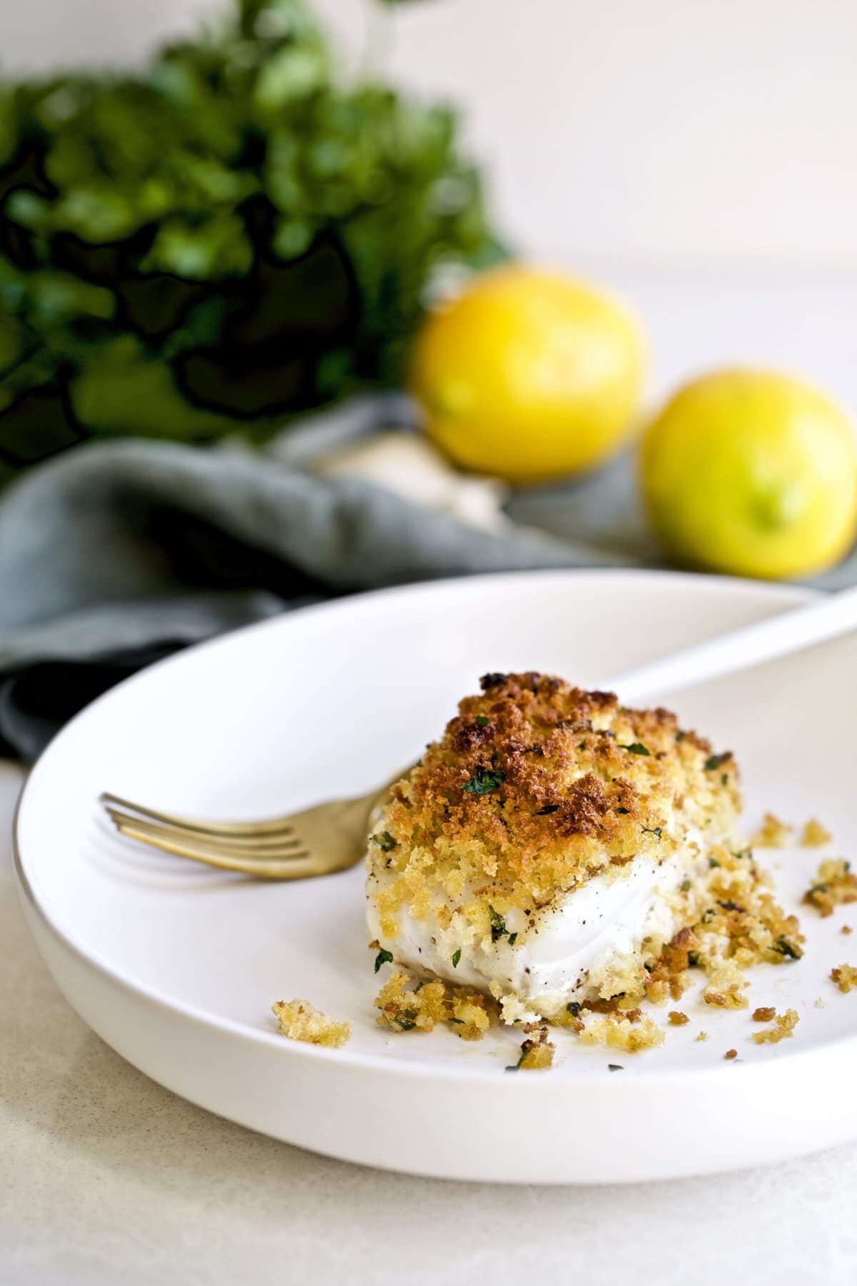Crispy Baked Cod with Panko Recipe on a plate with lemons, parsley, and garlic in the background