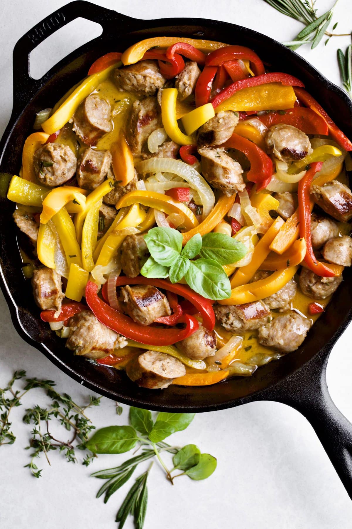 sausage and colorful peppers in a skillet. Herbs in background.