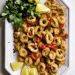 Plate of air fried calamari with lemon wedges and lemon slices.