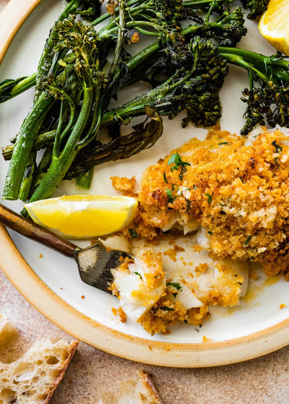 crispy baked cod with panko on a plate with broccolini. Bite taken out of fish.