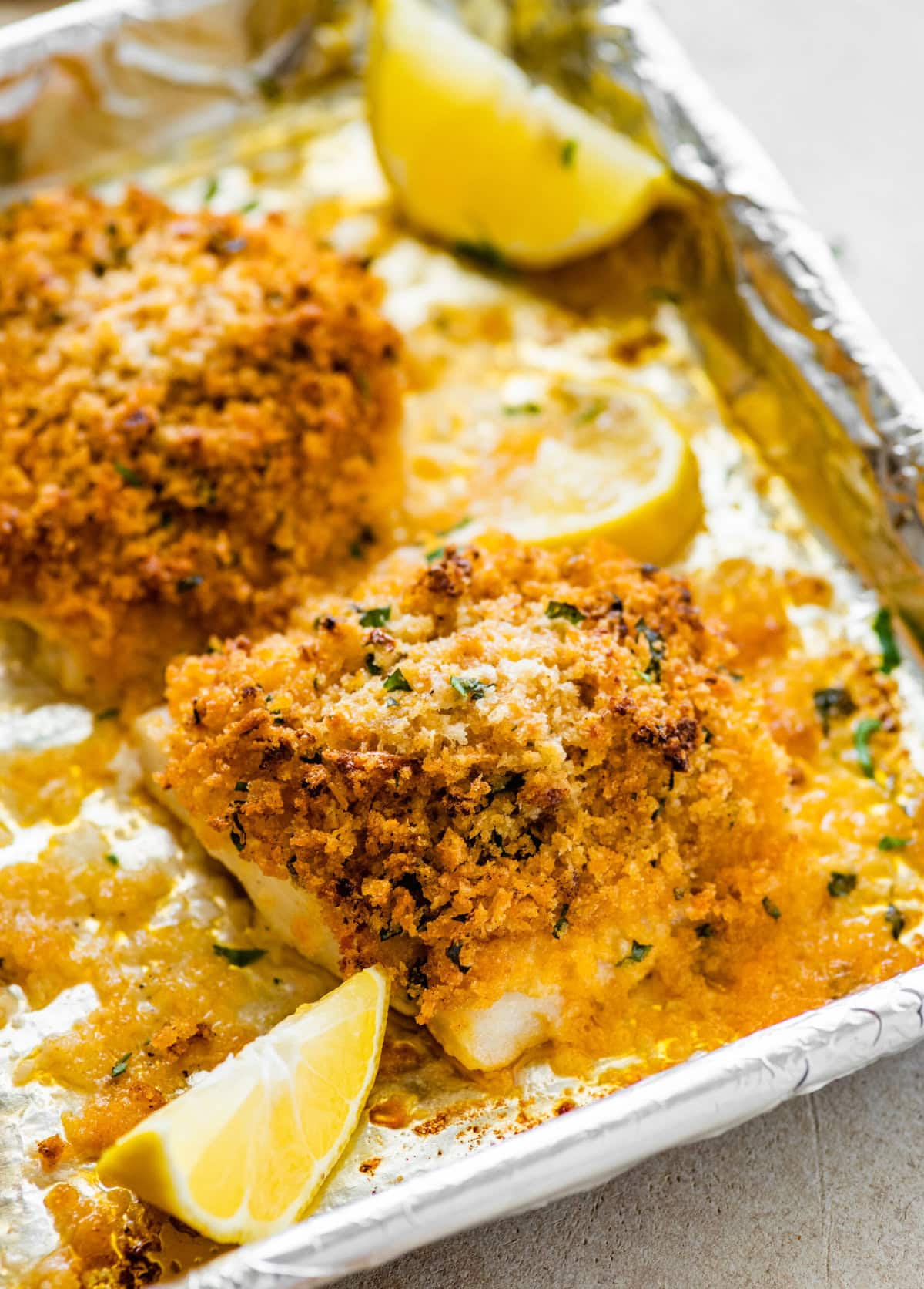 baked cod with panko after baking on the baking sheet. Lemons on the tray.