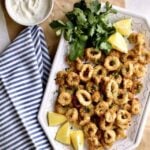 Plate of air fried calamari with lemon wedges and lemon slices side of sauce.