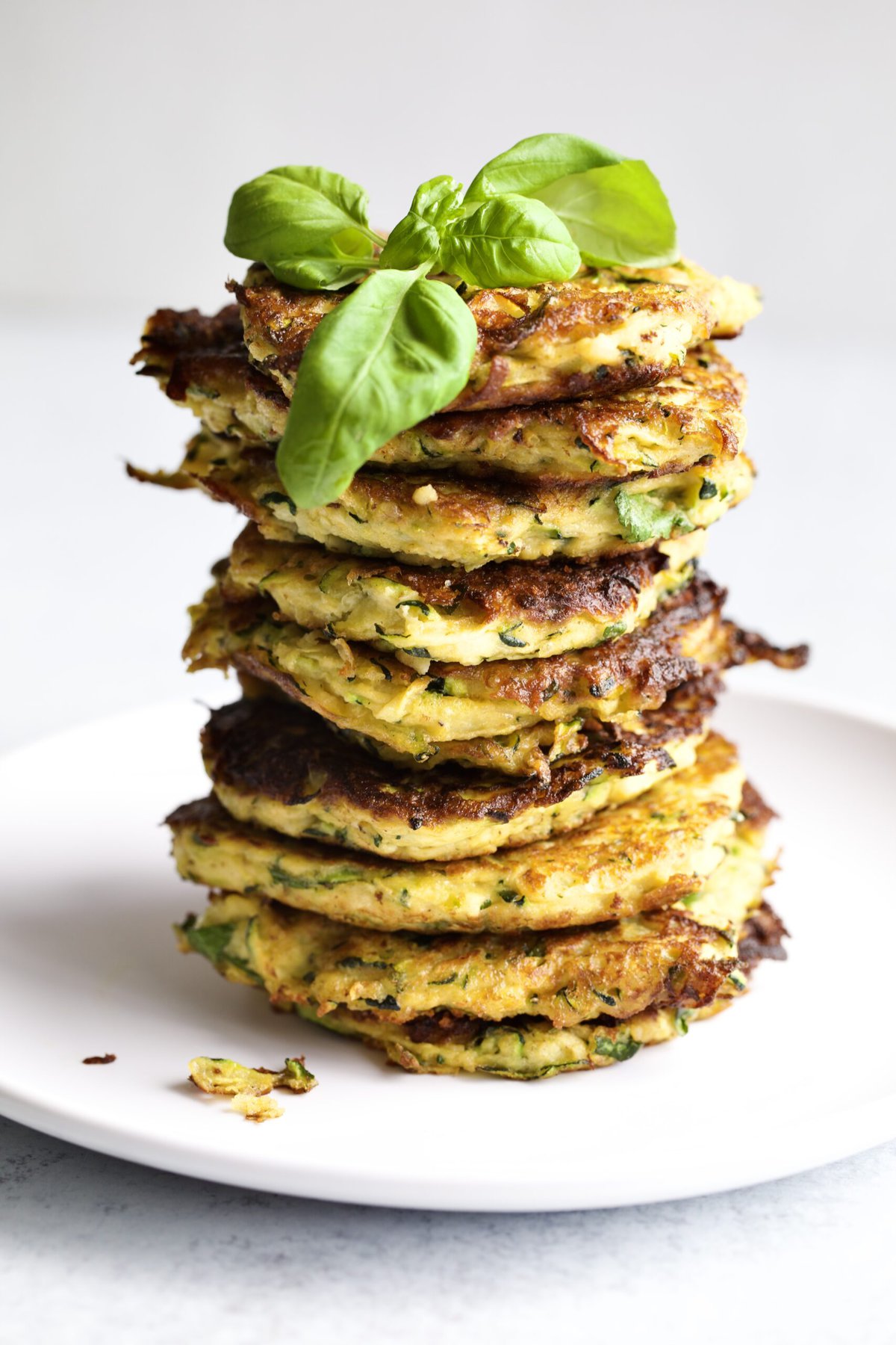 stacks of zucchini fritters on a plate. Basil leaf on top. 