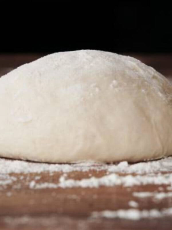 Homemade yeast dough ball for pizza on floured wooden table.