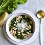 Bowl of Italian beans and greens next to a spoon.