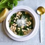Italian beans and greens soup in a bowl with a gold and white spoon.