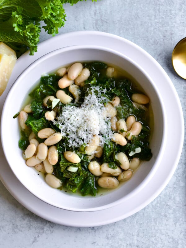 Italian beans and greens soup in a bowl with a gold and white spoon.