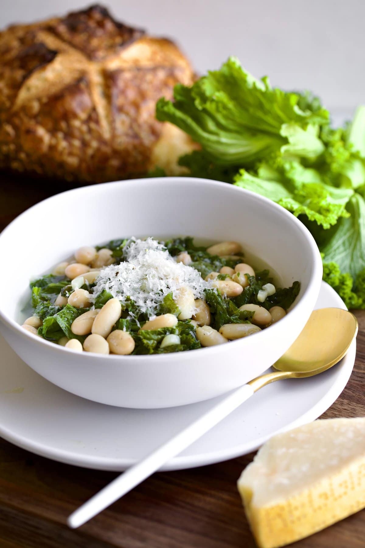 Italian beans and greens soup in a bowl with crusty bread and escarole leaves in background.