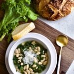 Italian beans and greens soup in a bowl on a wooden board with crusty bread .