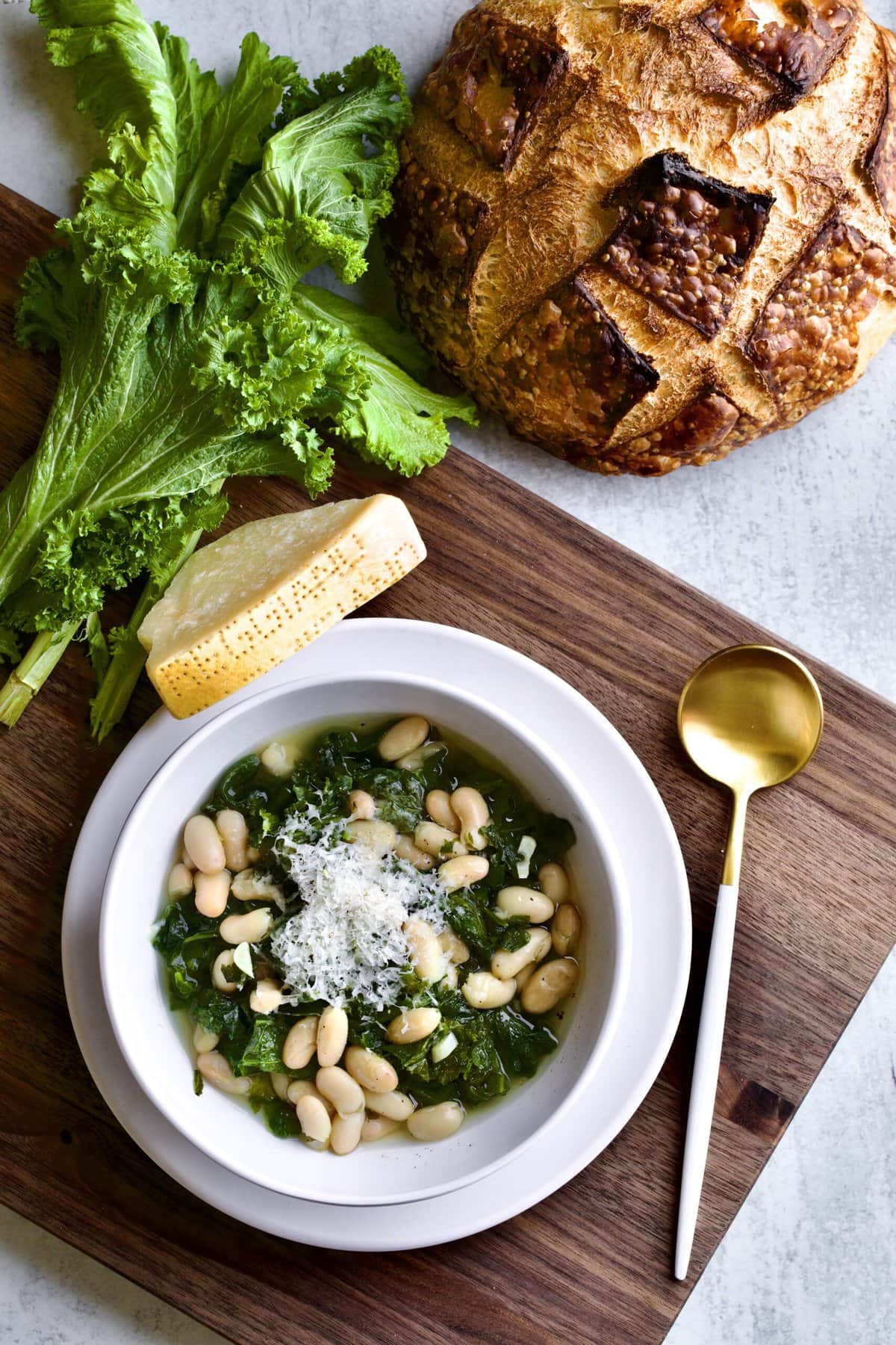 Italian beans and greens soup in a bowl on a wooden board with crusty bread .