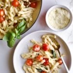 portion of gemelli pasta and tomatoes with mascarpone on a plate with a fork and pan in the background.