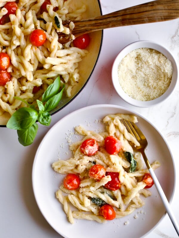 portion of gemelli pasta and tomatoes with mascarpone on a plate with a fork and pan in the background.