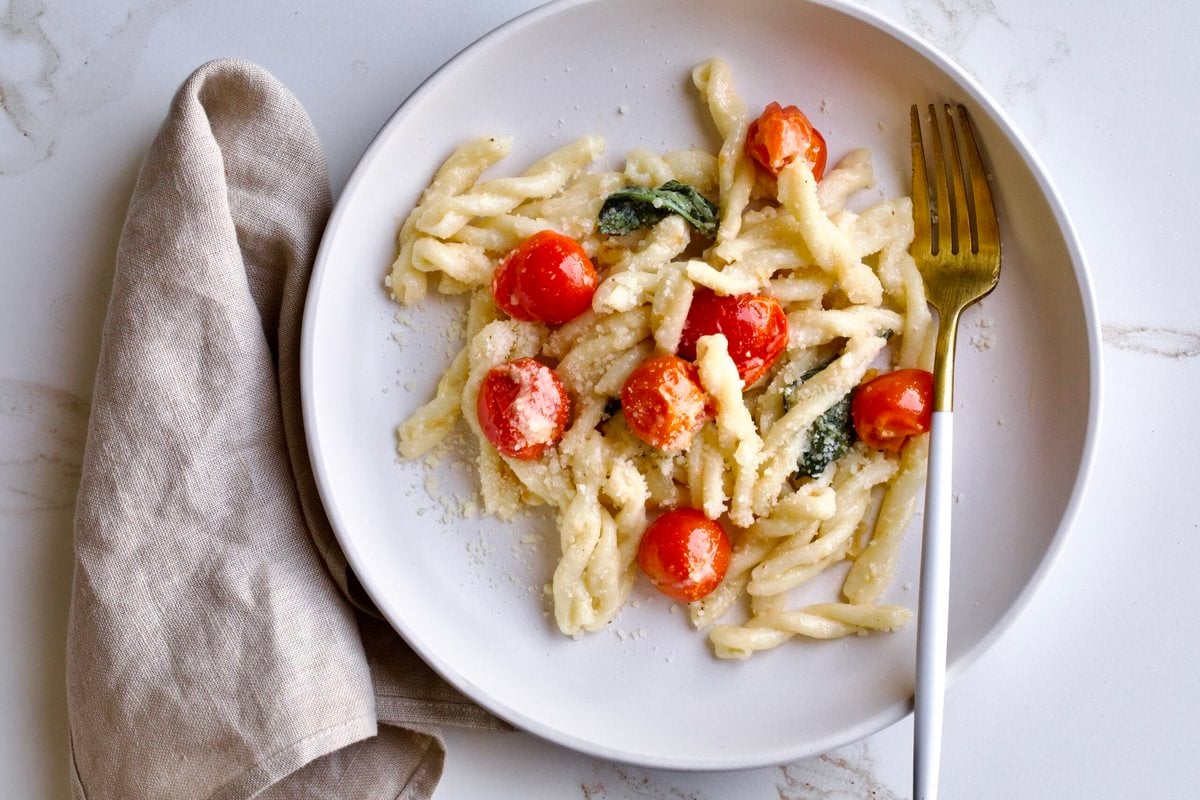 portion of gemelli pasta and tomatoes with mascarpone on a plate with a fork.