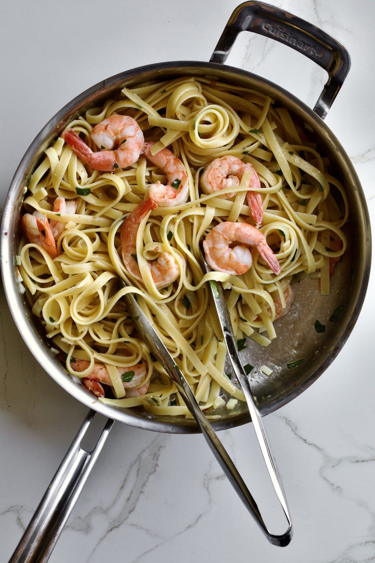 Shrimp scampi fettuccine in a pan ready to serve. with serving tongs.