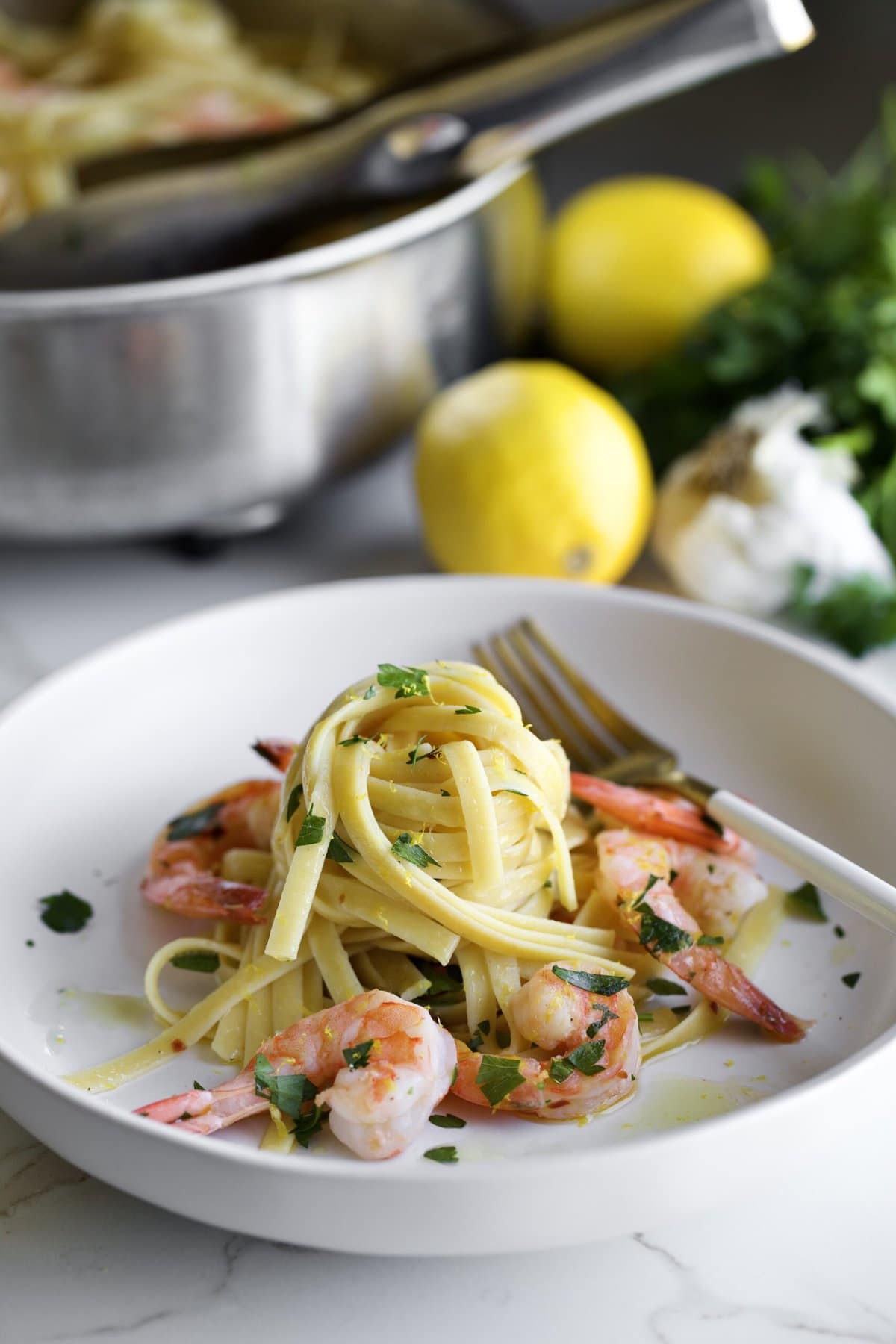 shrimp scampi fettuccine on a plate with parsley and a fork and serving pan in background.