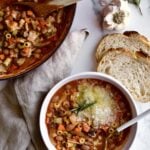 pot of pasta e fagioli with bread on the side and grey napkin.