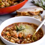 bowl of pasta e fagioli with red pot in the background.