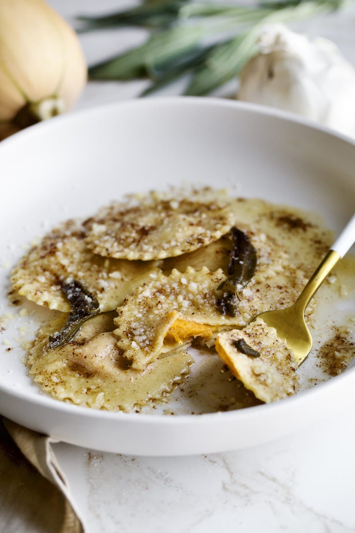 cooked butternut squash ravioli in sage brown butter sauce on a plate with fork bit taken out of one.